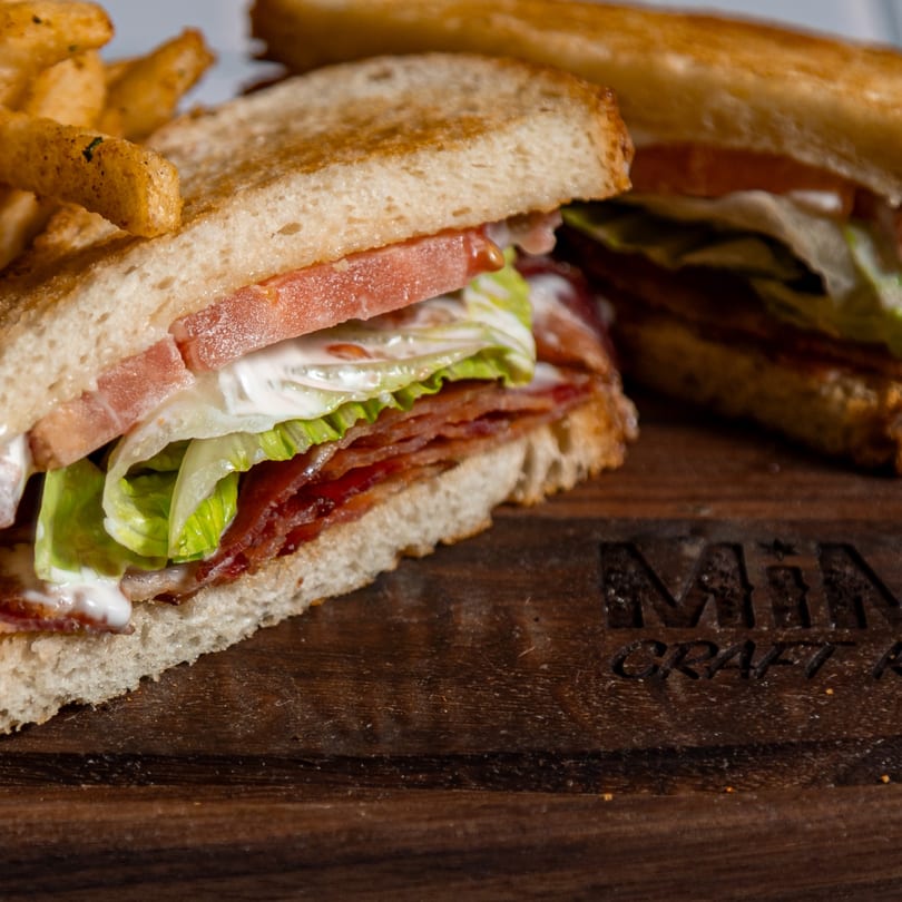 A MiMi's Craft Kitchen BLT sandwich with fries on a wooden board.