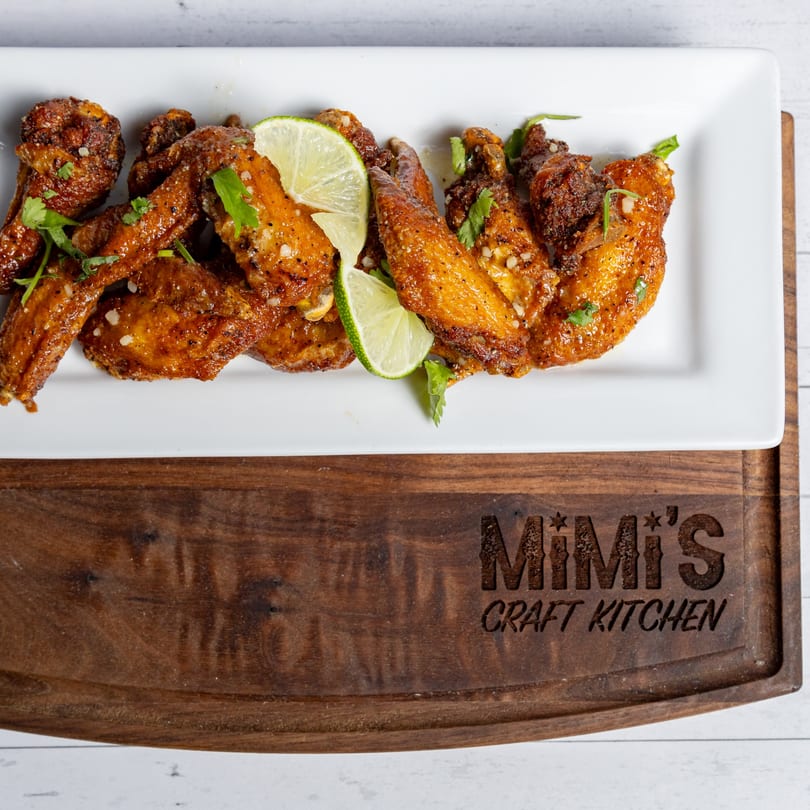 MiMi's Craft Kitchen's American chicken wings, garnished with lime and cilantro, on a white rectangular plate.
