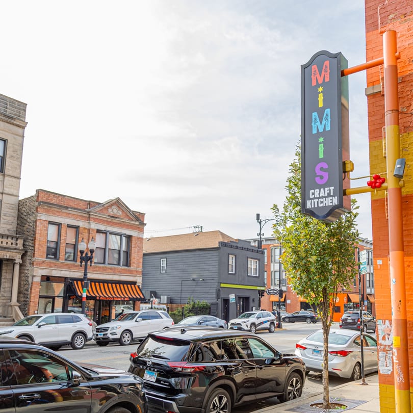 MiMi's Craft Kitchen sign on a brick building, with parked cars and other buildings lining a city street.